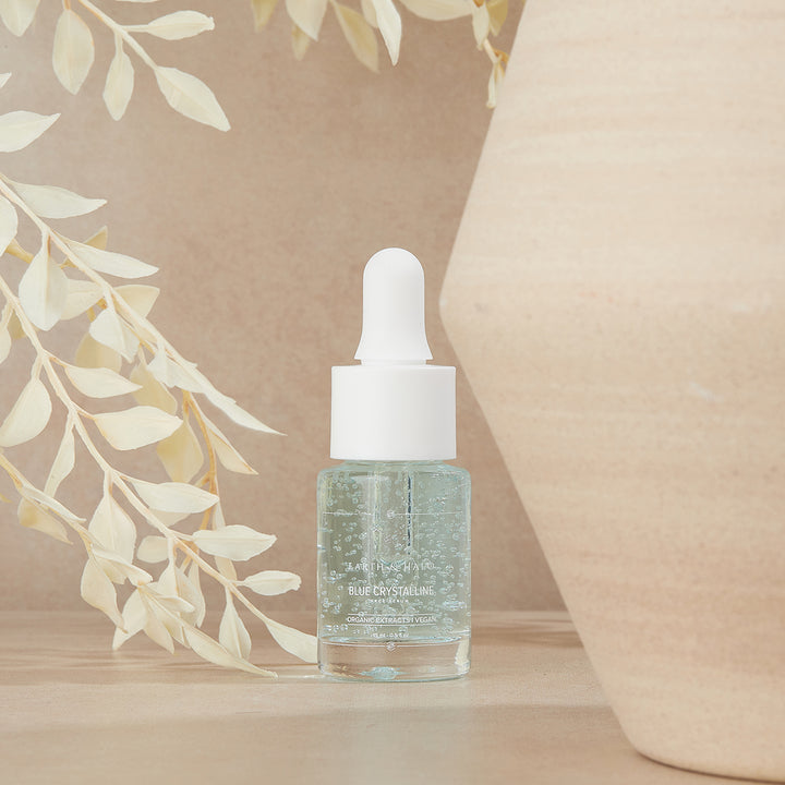 Blue Crystalline Face Serum 15 ml dropper bottle beside pale foliage and a beige vase