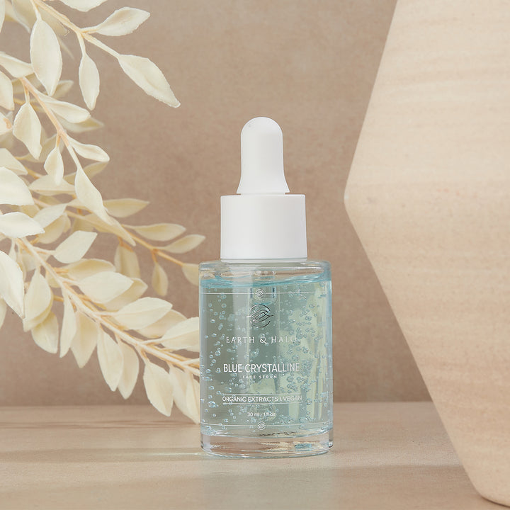 Earth & Halo Blue Crystalline Face Serum 30 ml dropper bottle on a beige pedestal